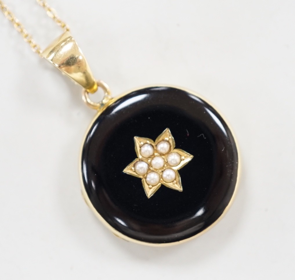 A late Victorian 15ct, black enamel and seed pearl set circular mourning locket, diameter 23mm, on a 9ct fine link chain, 40cm, gross weight 10 grams.